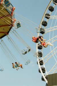 People enjoying swing ride and ferris wheel under blue sky.